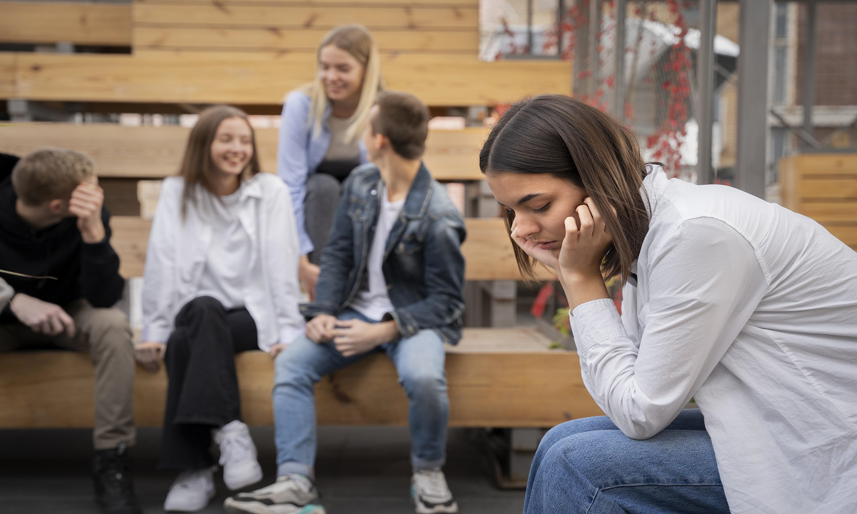 A girl sitting alone while her friends are sitting together and enjoying.